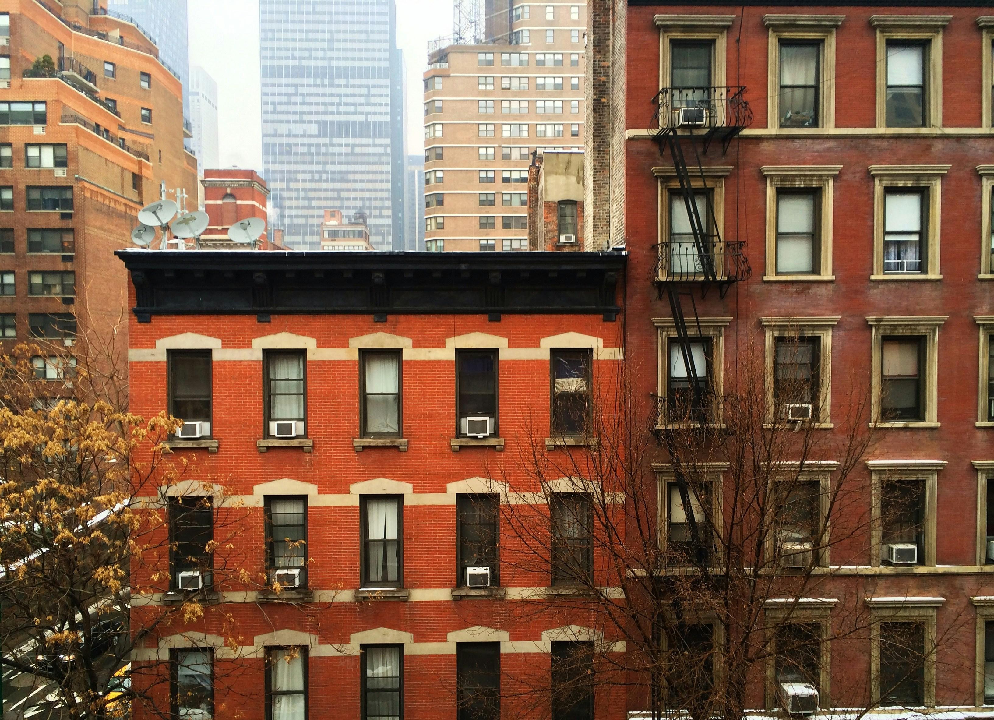 Red-brick NYC apartment buildings with dozens of window air conditioners visible across the facade