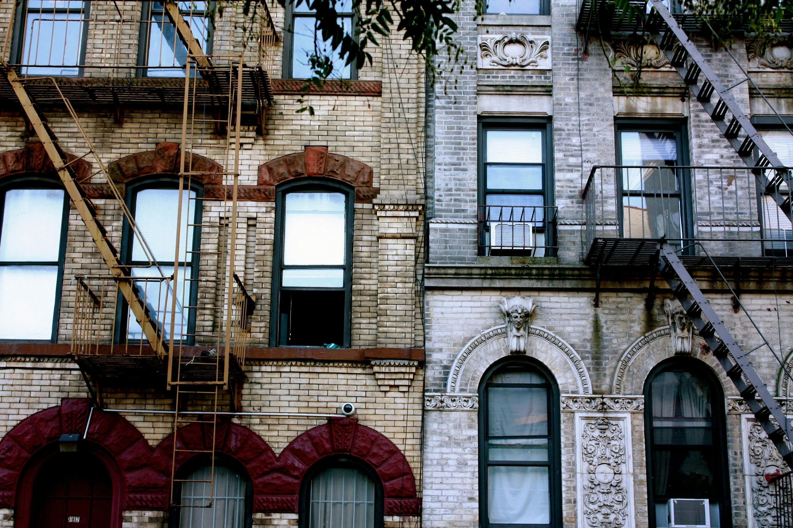 Black-and-white photo of two adjacent NYC tenements with painters' ladders and visible window air conditioners