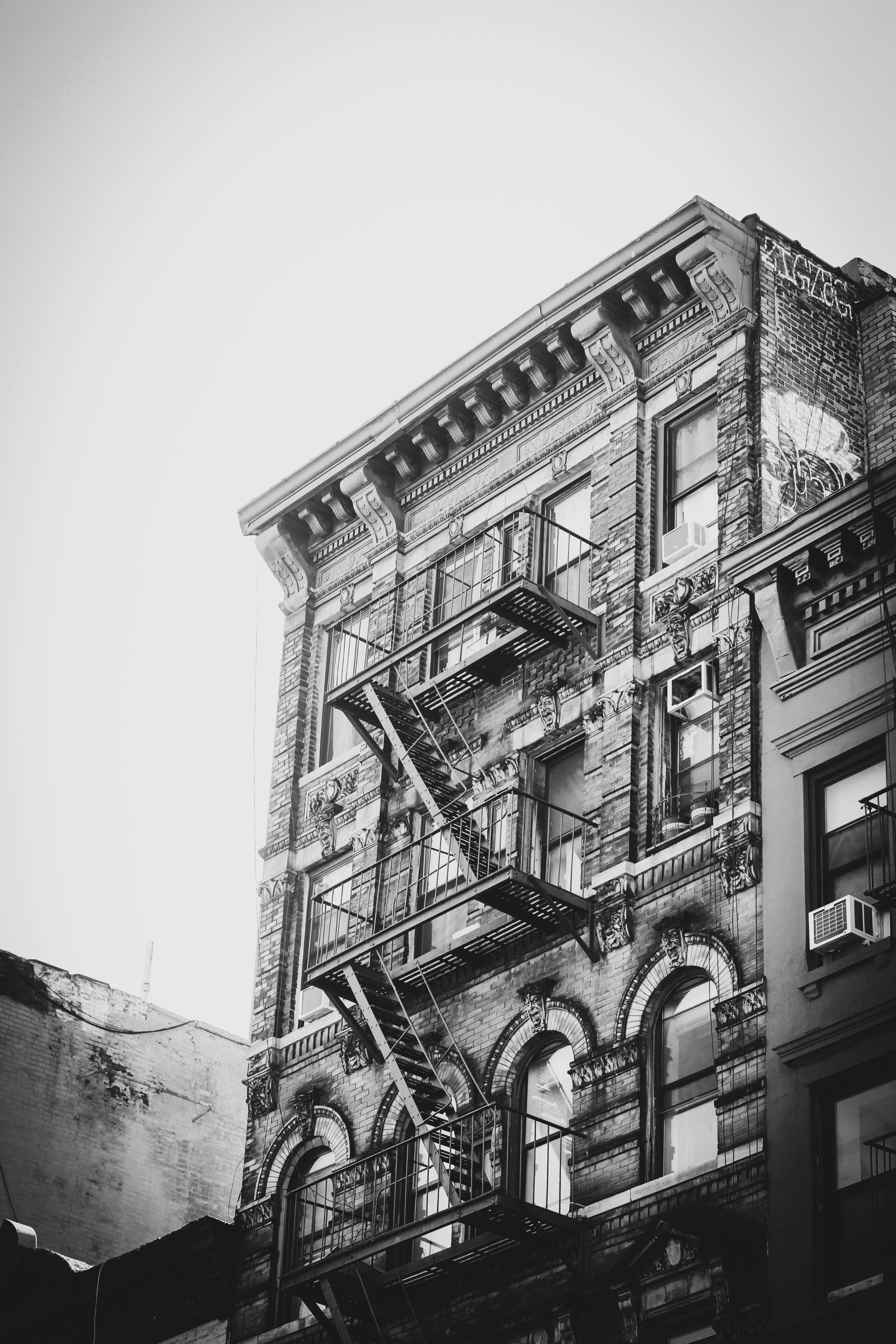 Black-and-white NYC tenement with a window air conditioner installed mid-floor and a zig-zag iron fire escape