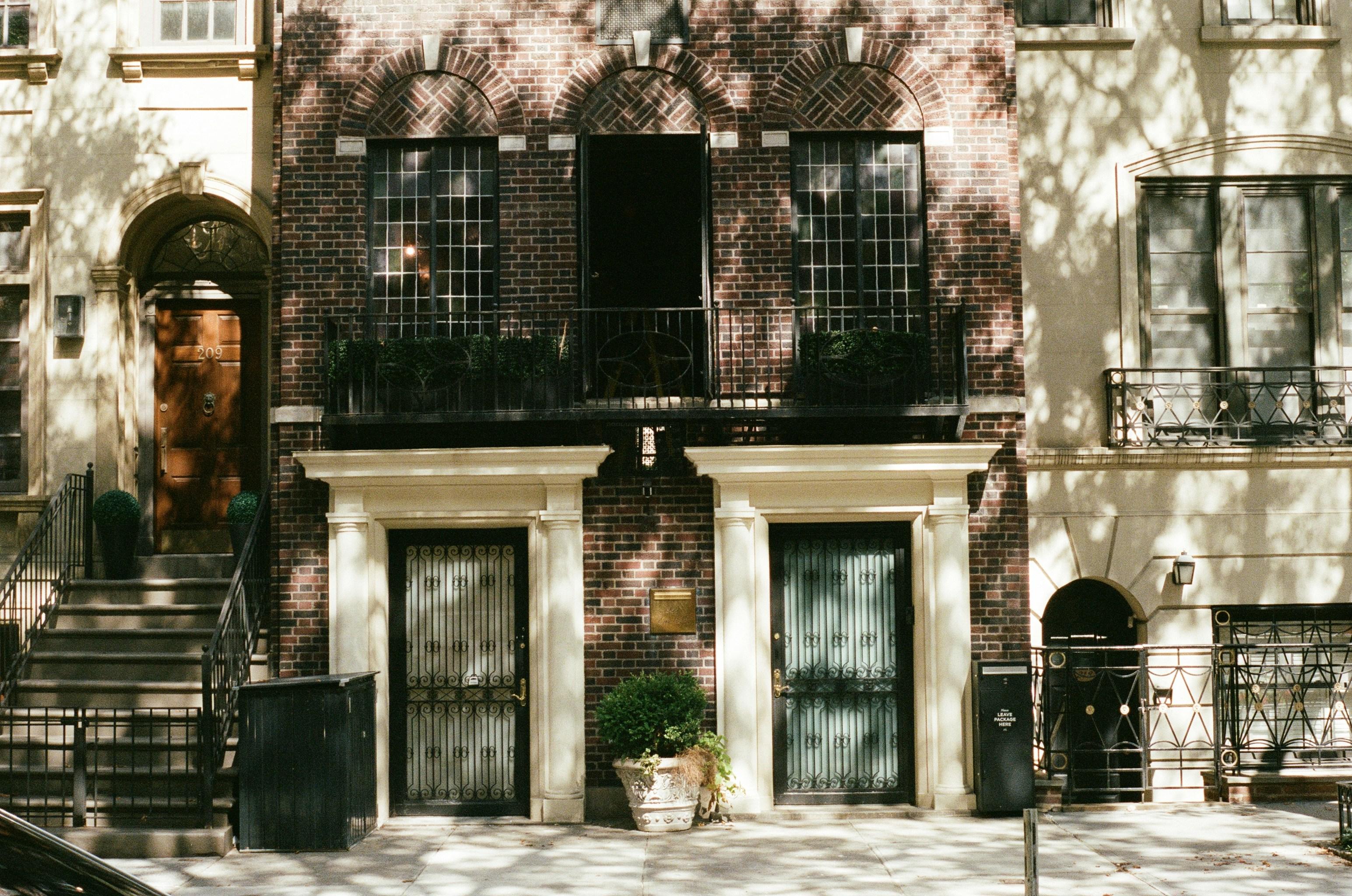 Greenwich Village brick townhouse with twin doorways and dappled tree shadows on the brick facade