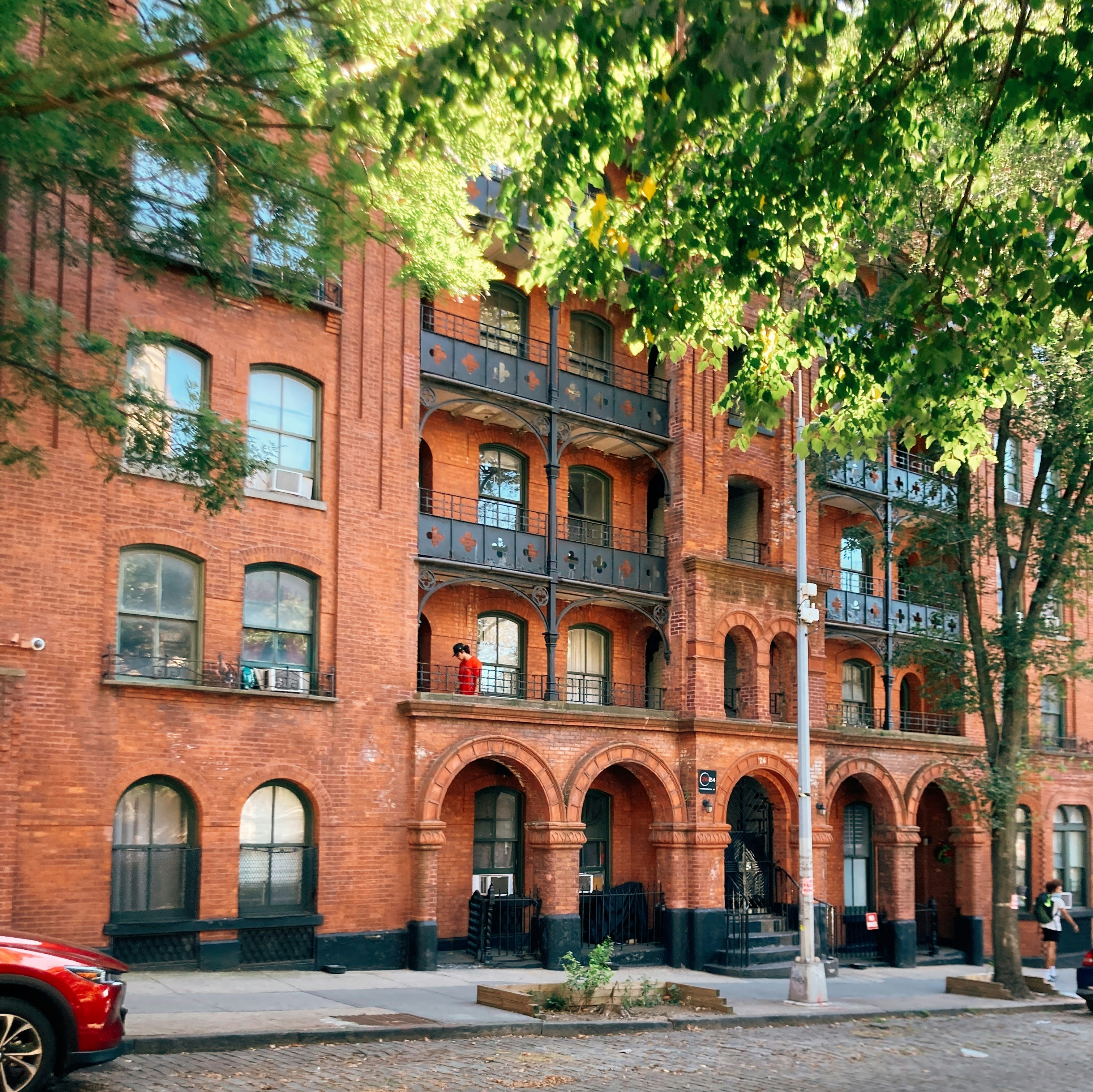 Red brick NYC walk-up with arched entryways, balustrades and decorative cornice, framed by green leaves